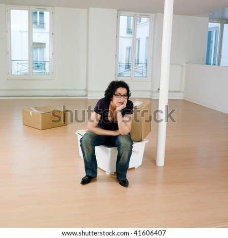 man sitting on the floor inside an empty loft apartement with tax forms and laptop computer
