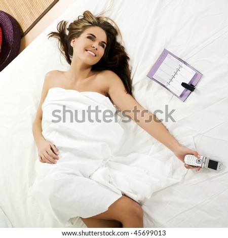 beuatiful caucasian woman lying on a white bed with a telephone in her hands