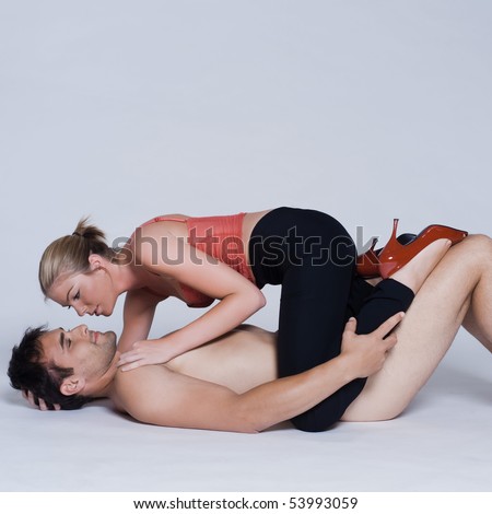 young couple lying down with woman on top and man naked in studio on isolated grey background