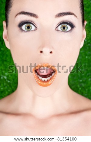 Closeup portrait of a beautiful surprised woman with wide open green eyes and glossy lips on green