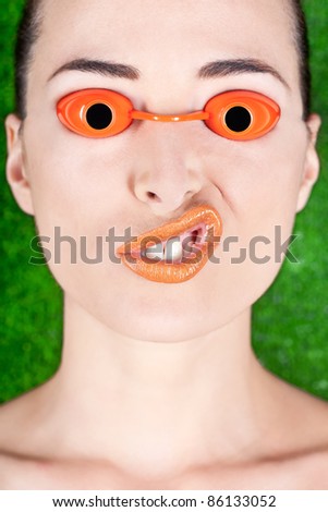 Closeup of a beautiful woman wearing tanning bed glasses and pulling a strange face isolated on green
