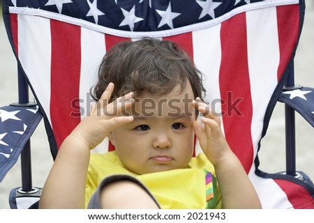 young asian boy sits in american flag chair playing peekaboo