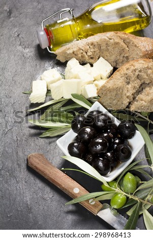 Mediterranean olives with feta cheese, virgin extra oil and fresh bread over dark stone