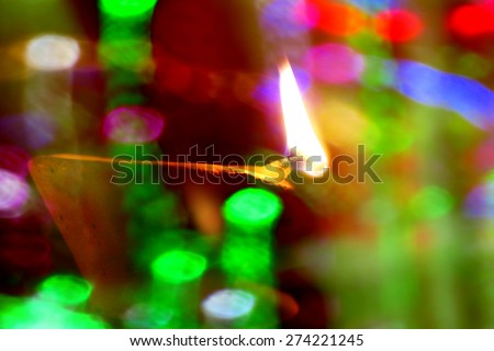 A traditional earthen Diwali lamp lit behind a string of colorful light bulbs in blur