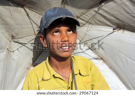 A poor Indian boy with an umbrella desperately waiting for the rains during the hot Indian summer.