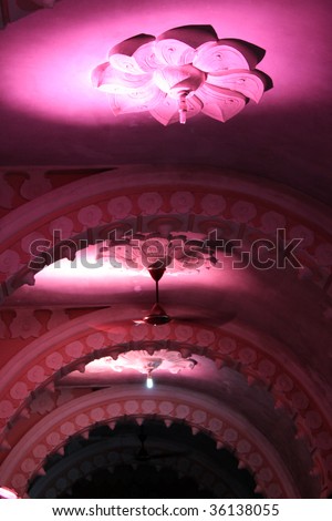 The beautiful ceiling of a royal Indian hall with traditional floral designs, lit in pink lights.