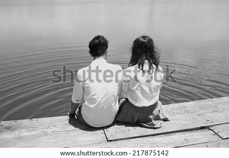Rear view of man and woman couple sitting at the lake, black and white