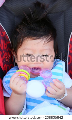 Five months baby girl chews on a soft plastic toy in the stroller