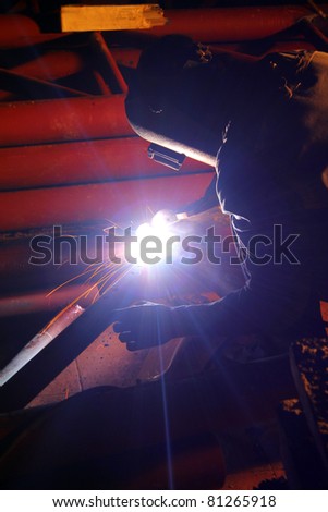 Welder with welding helmet working hard, sparks and smoke around him