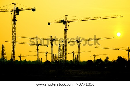Industrial construction cranes and building silhouettes with sunrise