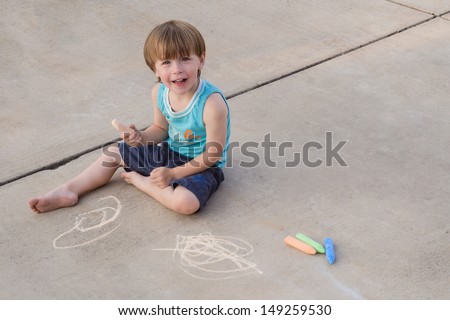 A three-year old sidewalk chalk artist sits on a light colored pavement. Space at the side for text copy.