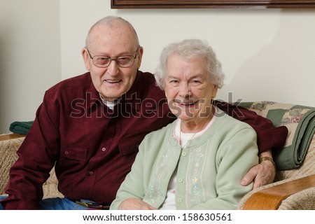 Casual close-up portrait of a happy elderly couple in their eighties sitting on a sofa in their living room.