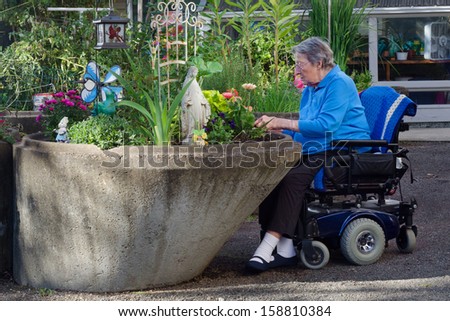 An elderly woman in an assisted-living facility tends to her flowers in a wheelchair-accessible garden.
