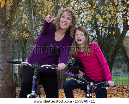A pre-teen girl looks as her mother points to something in the distance, perhaps a bird or animal, as they stop on a fall bike ride.