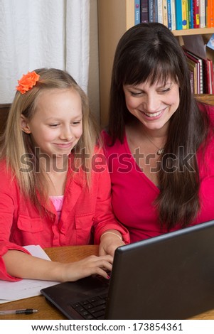 A mother and her young daughter are amused as they view a laptop screen together; perhaps Skyping with her father - or maybe just watching cat videos.