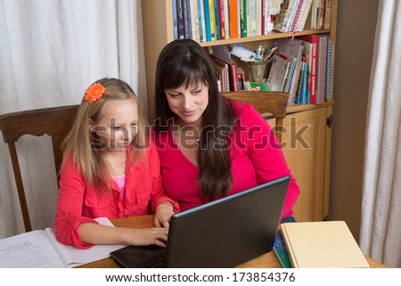 A mother and daughter share time together while using a laptop to do her home\
work.