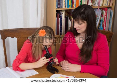A mother homeschools her daughter as she learns about science while using a microscope