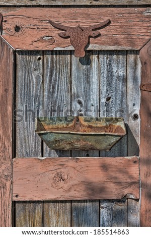 The rusty silhouette of a western steer head is nailed to the weathered door of a shed with a rusted out metal container nailed below it in an artistic garden art collage.