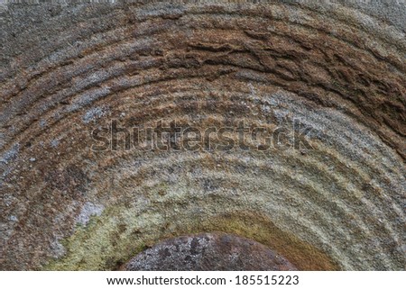 Detail of an old western grinding stone makes a circular pattern in gritty shades of rust, grey, and ochre.