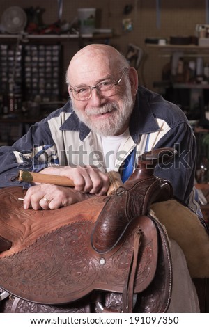 A smiling, happy leather craftsman in his eighties in a portrait with dramatic lighting.