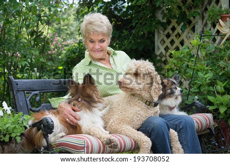 A ninety year-old elderly woman shares a garden bench and companionship with her three dogs.
