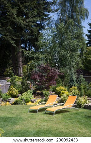 A pair of bright yellow designer lawn chairs invite you to relax in this beautifully landscaped backyard with tall trees in the background.