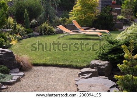 A pair of bright yellow designer lawn chairs invite you to relax in this beautifully landscaped backyard.