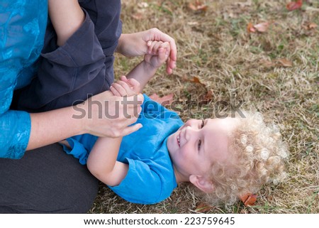 Attention is centered on the happy expression of a curly headed toddler as he looks at his mother, who is out of the frame