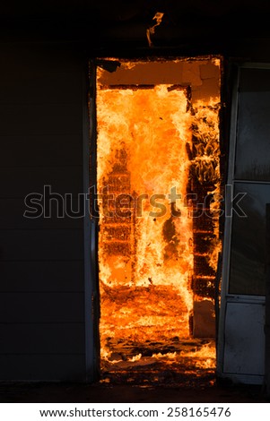 A raging fire consuming the inside of a home as viewed through a dark doorway
