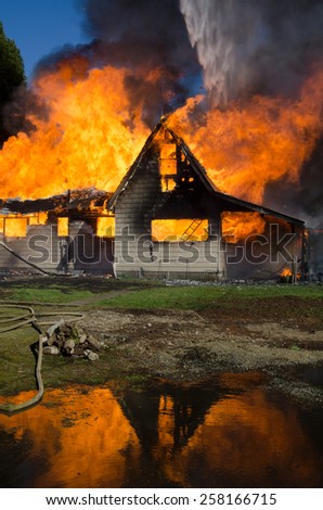 The blaze of a burning house is reflected in a pool of runoff from fire hoses.