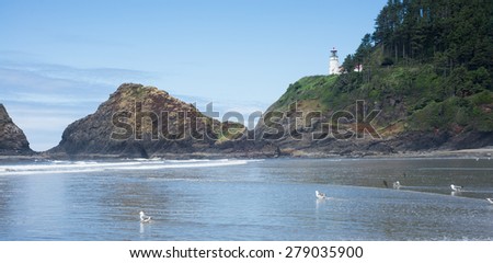 The Heceta Head lighthouse perches high on a cliff above craggy rocks and a water covered beach in Lane County Oregon.