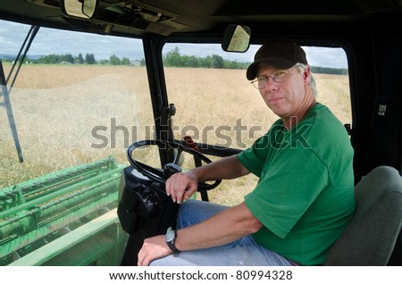 A serious farmer sits in his cab with a grass seed field seen through the window.