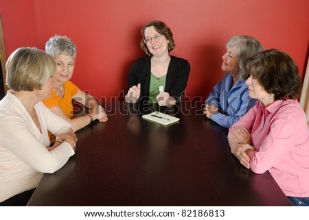 Looking down at four senior woman sitting around a table with a younger woman leading a discussion.