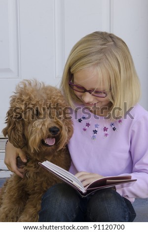 Close-up of a young pre-teen girl with her arm around her dog reading by her front door.