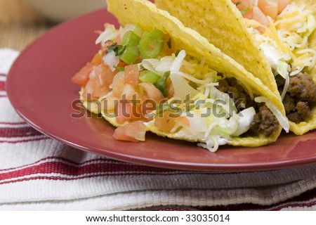 closeup of beef tacos with cheese, lettuce, diced tomatos on a red plate