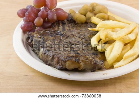 grilled tbone steak with french fries, fried okra and fresh grapes on a beige plate