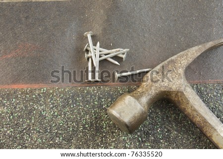 green asphalt shingle lined up on orange chalkline with roofing nails and worn hammer