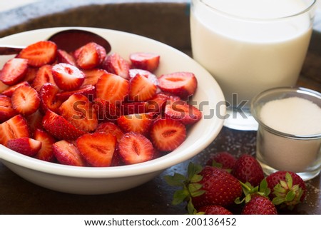Strawberries in a bowl with milk and sugar on an old wooden textured plate