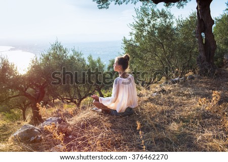 Yong women in olive field meditating  toward the sea on sunset