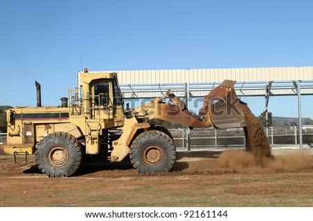 Front loader spreading dirt across the ground at a rural building site.