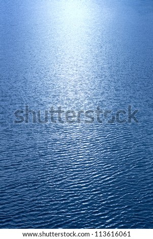A beam of sunlight reflecting over rippled blue water