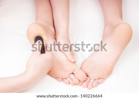 Therapist doing a foot massage, pressing reflexology zone on woman\'s heel with a hot stone