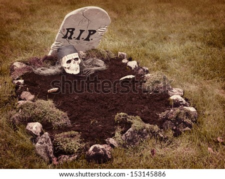 Skull with hands reaching from the grave. Decoration in a garden for halloween