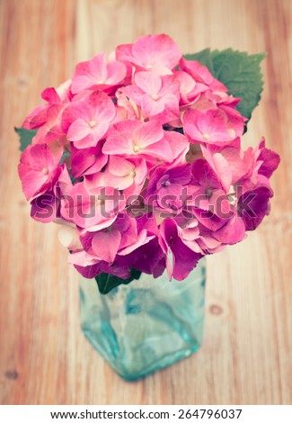 A light pink hydrangea flower in a a blue transparent vase on a vintage retro background