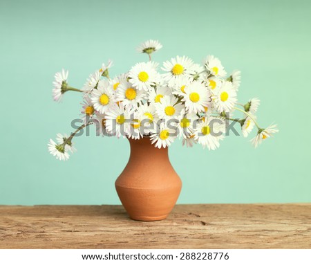Retro daisy\'s flowers in a brown ceramic pot on a solid wood surface