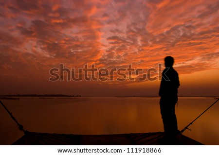 Dramatic golden orange sunset with a silhouette of a man, over Asia\'s largest salt water lake in Chilika, India