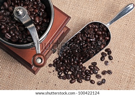 Photo of a hand operated traditional coffee grinder with a scoop full of arabica beans on a hessian background.