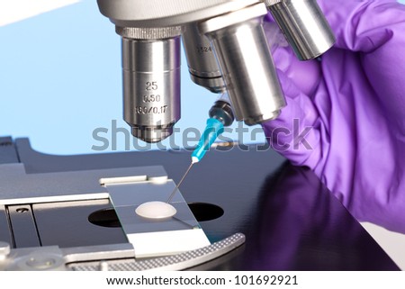 Photo of a sperm sample on a microscope slide with a syringe being used to extract an embryology specimen for analysis.