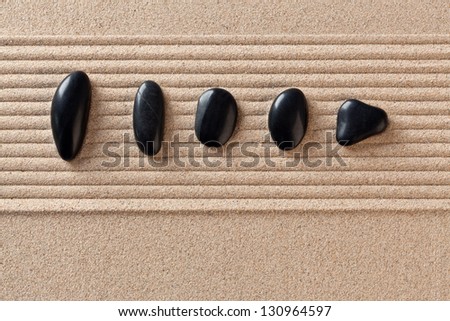 Five black pebbles on a raked sand zen garden.