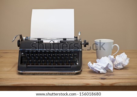 An old retro typewriter with a piece of blank paper for you to add your own text, coffee mug and two pieces of screwed up paper besides it on the desk.